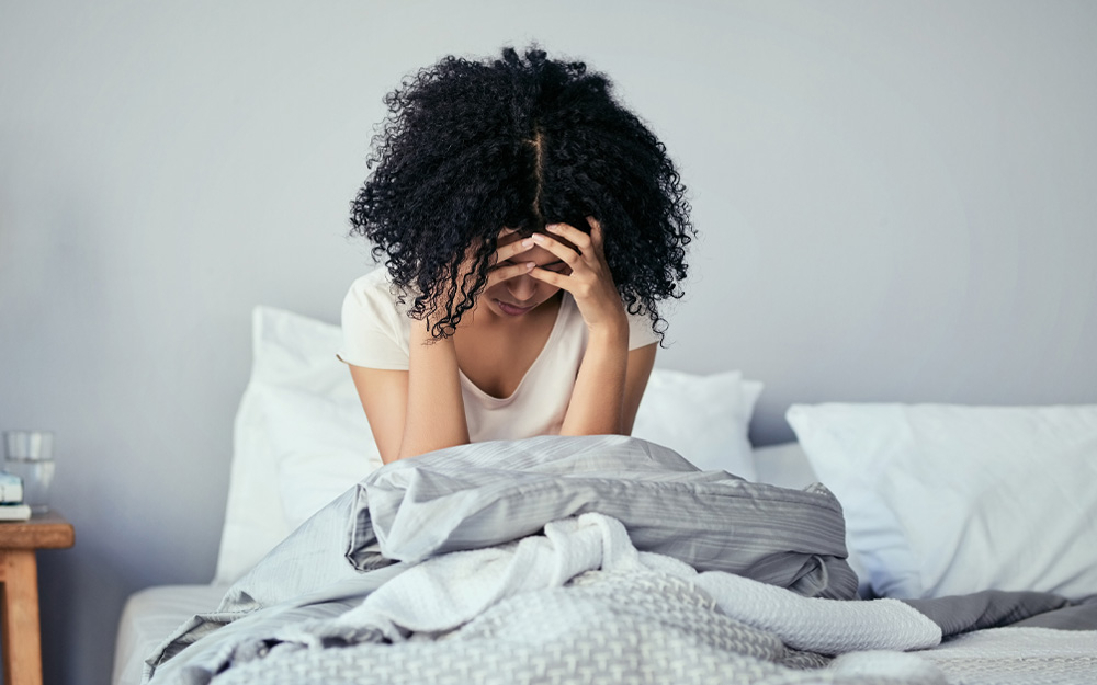 Woman in bed holding her head in pain.